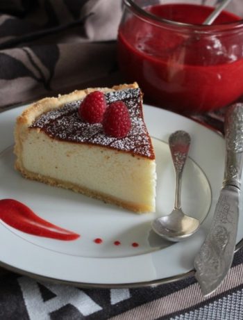 Part de tarte au fromage blanc avec framboises et coulis rouge sur assiette blanche
