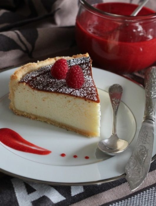 Part de tarte au fromage blanc avec framboises et coulis rouge sur assiette blanche