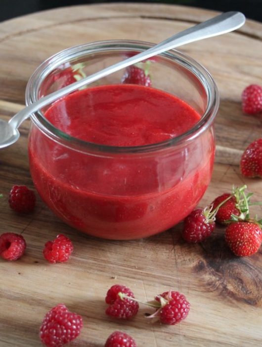 Pot de coulis de framboise rouge vif entouré de fraises et framboises fraîches