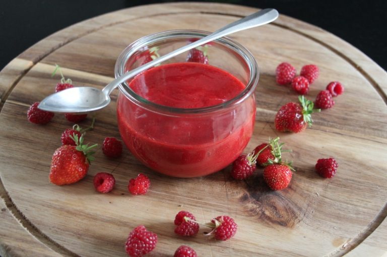 Pot de coulis de framboise rouge vif entouré de fraises et framboises fraîches