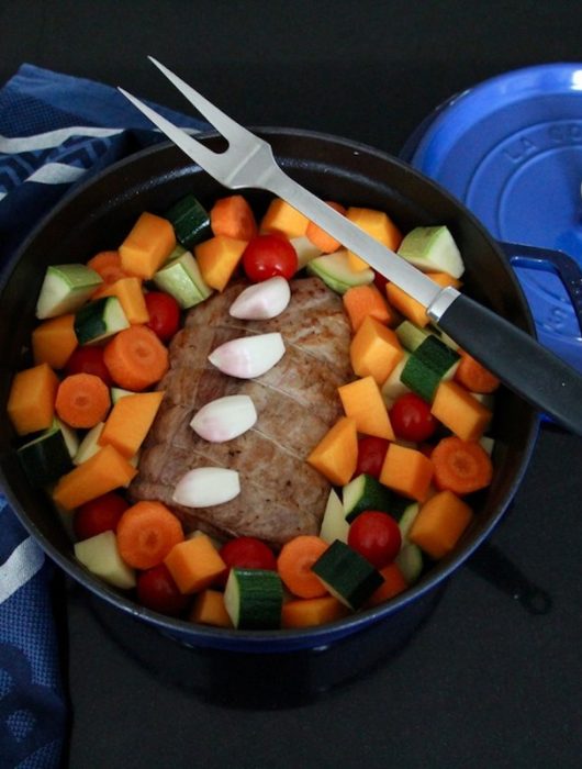 Rôti de porc en cocotte entouré de légumes colorés dans une cocotte bleue