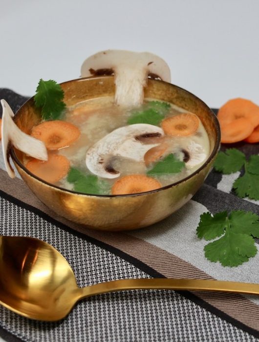 Bol doré de bouillon thai avec champignons, carottes et coriandre