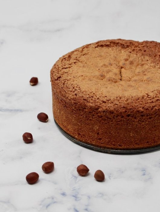 Gâteau au yaourt et noisettes doré, entouré de noisettes entières sur fond marbré