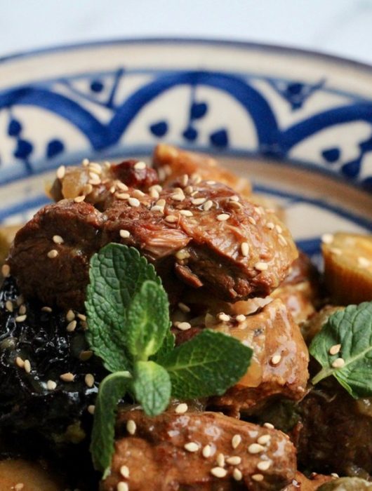 Tajine agneau aux pruneaux garni de menthe et graines de sésame dans un plat marocain