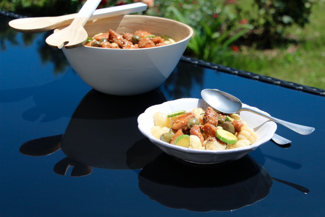 Bowl of pasta salad with soy chicken and zucchini, served outdoors in the sunshine