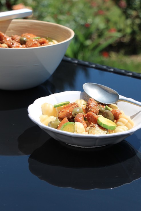 Bowl of pasta salad with chicken, zucchini, and olives outdoors