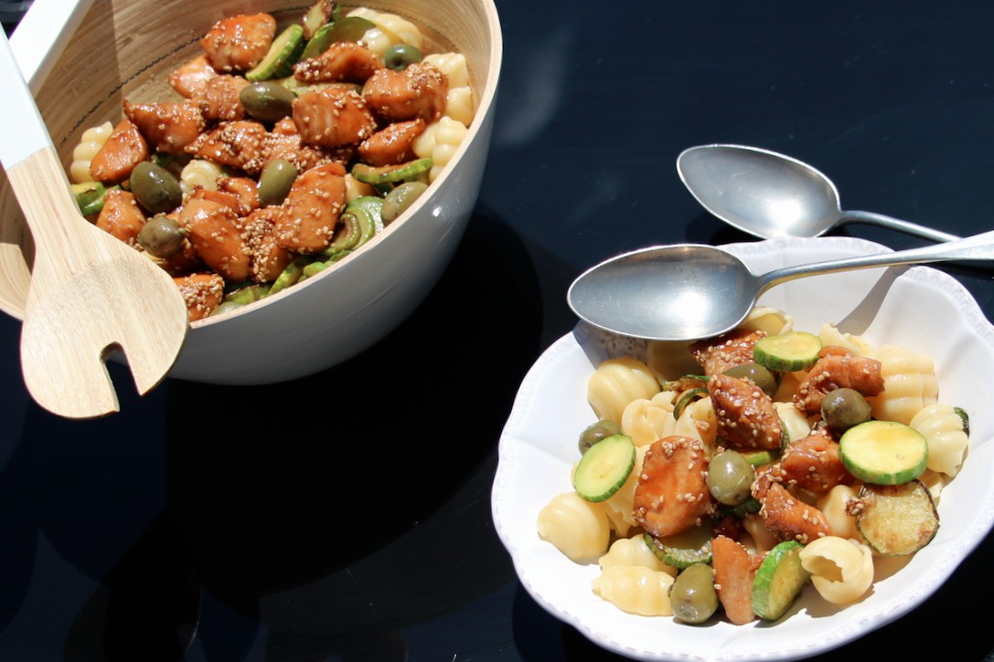 Wooden bowl filled with pasta salad featuring chicken, zucchini, and olives, with a simple setup