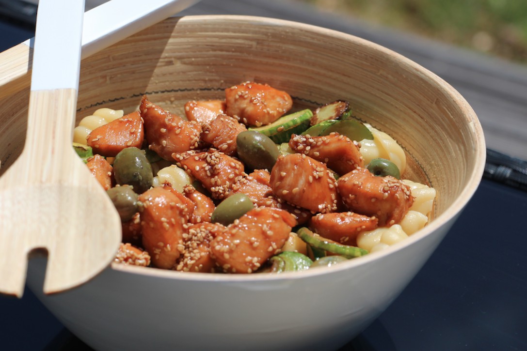 Golden browned chicken pieces, zucchini, and pasta in a wooden bowl