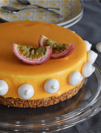 Entremet mangue passion sur assiette, nappage brillant, décoré de meringues blanches et fruits