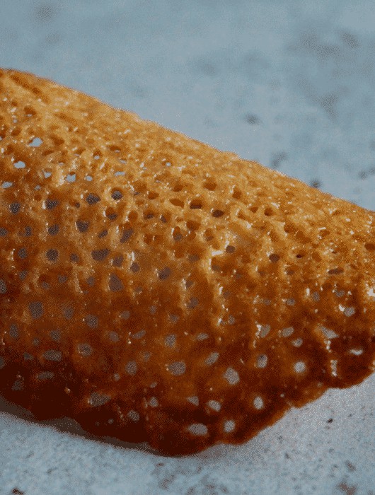 Tuile dentelle dorée en gros plan, texture ajourée sur fond gris