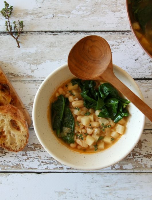 Rustic Tuscan white bean soup with wilted spinach, served in a speckled ceramic bowl with toasted bread on a wooden board