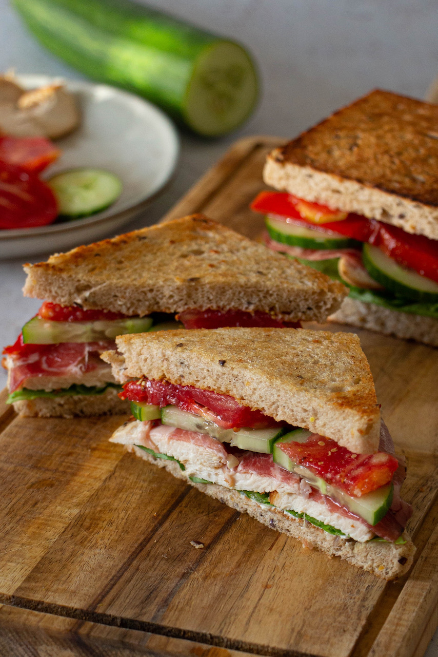Triangle-cut chicken sandwich showing layers of tomatoes and cucumbers