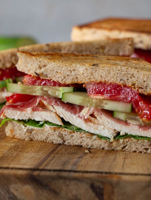 Sandwich poulet garni de concombres et tomates sur planche en bois