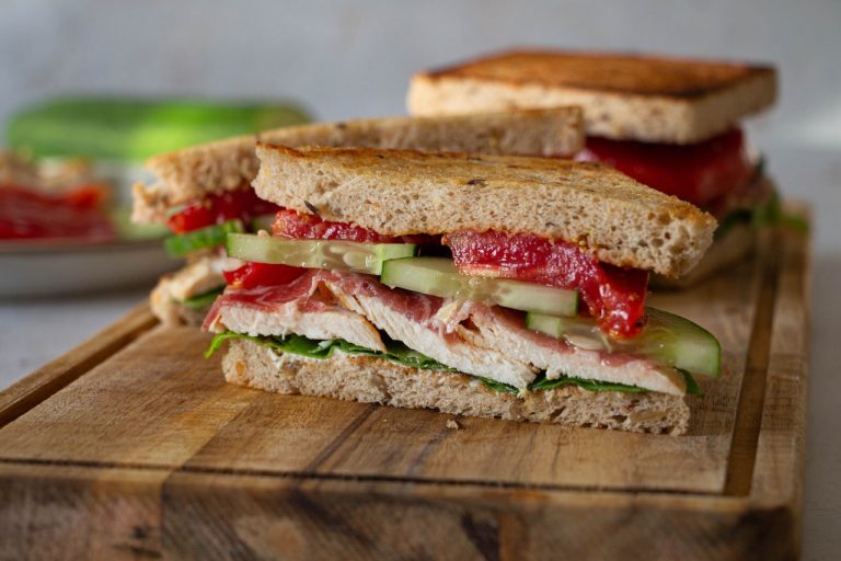 Sandwich poulet garni de concombres et tomates sur planche en bois