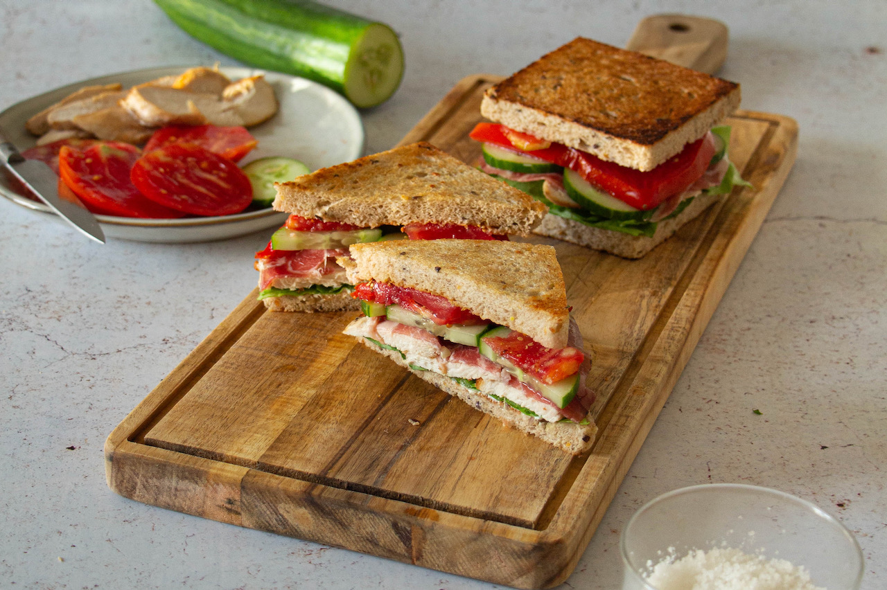Slices of chicken sandwich filled with fresh vegetables on a wooden board