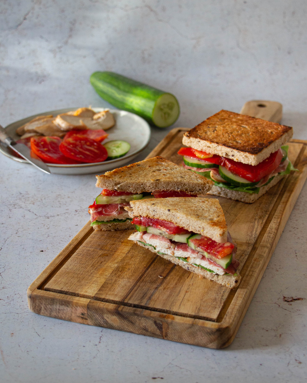 Chicken sandwich garnished with tomatoes and cucumbers on a wooden board