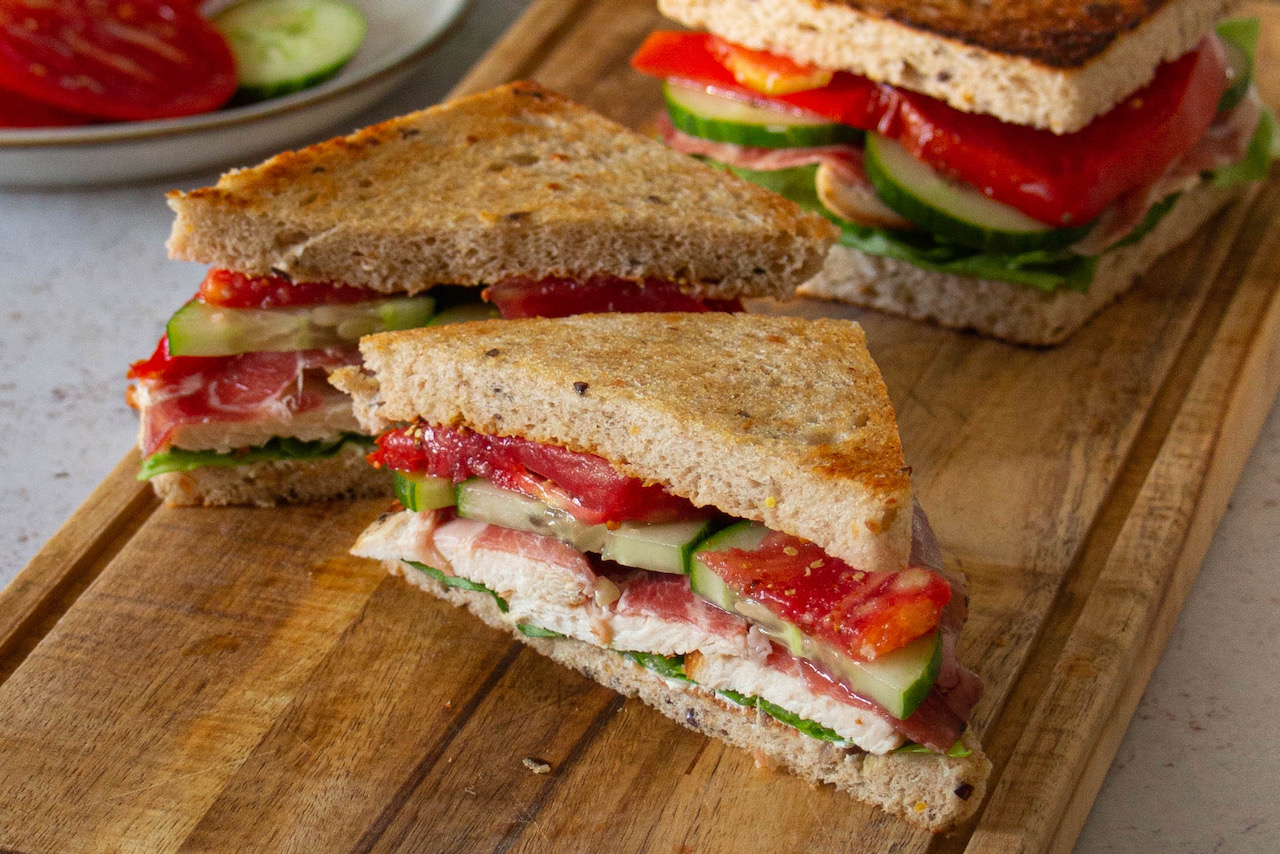 Slices of chicken sandwich filled with fresh vegetables on a wooden board
