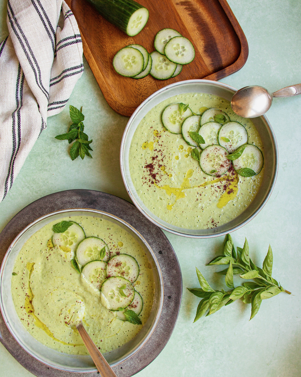 Two bowls of cucumber gazpacho garnished with cucumber slices and fresh mint
