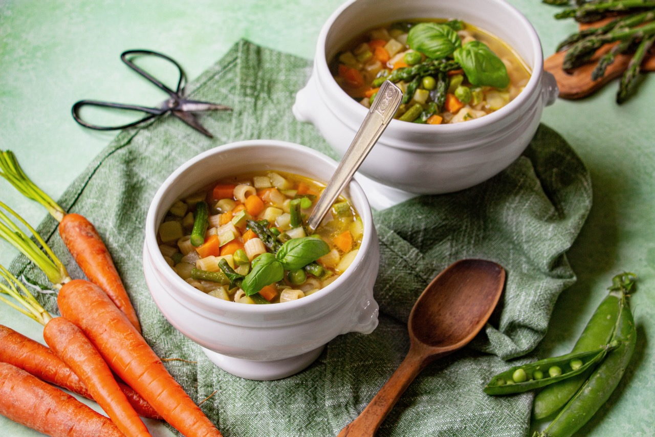 Two bowls of colorful minestrone, a spring dish for friends, on a green tablecloth
