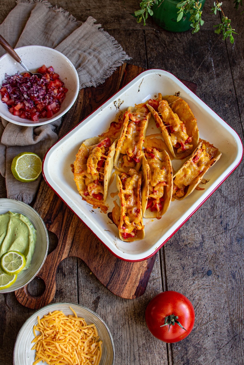 Gratiné Mexican chicken tacos in a white dish on a wooden table