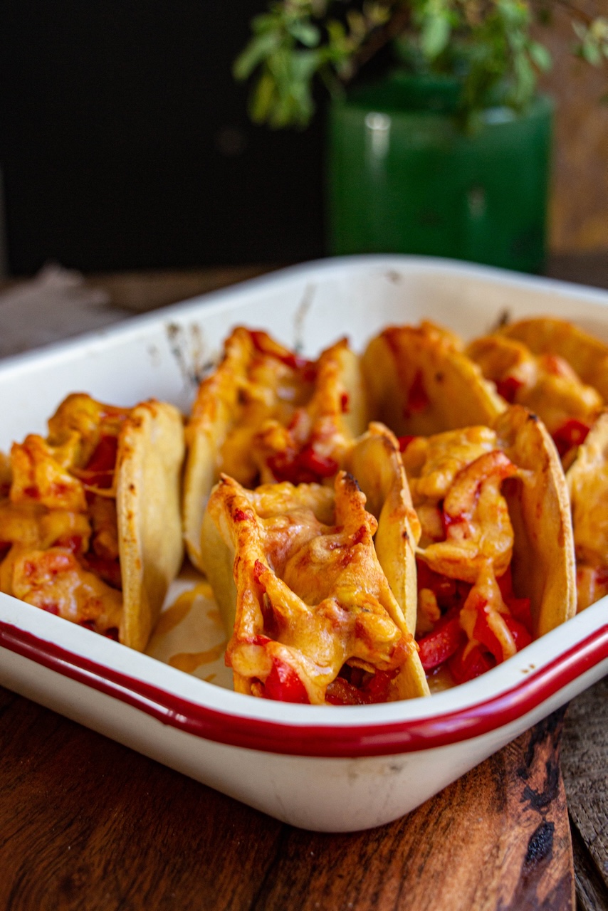 Gratiné Mexican chicken tacos, garnished with red peppers, in a white dish