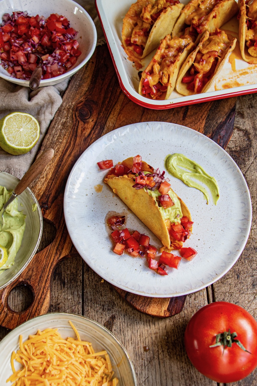 A taco garnished with chicken, tomatoes, and green sauce on a white plate