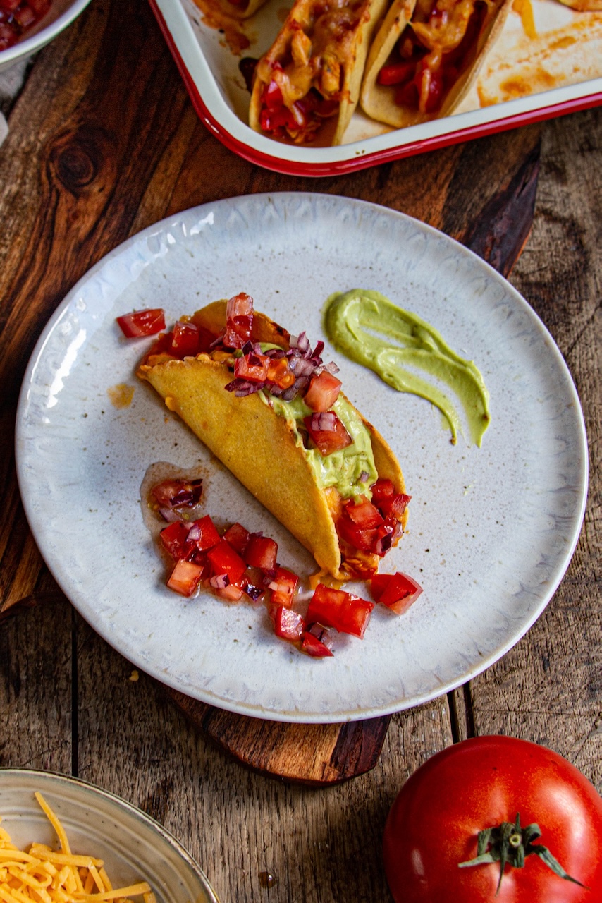 A taco filled with chicken, guacamole, and colorful salsa on a white plate