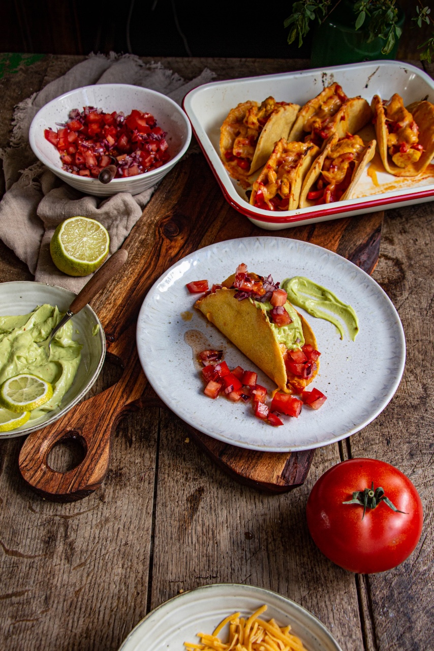 Mexican chicken tacos topped with salsa and guacamole on a white plate