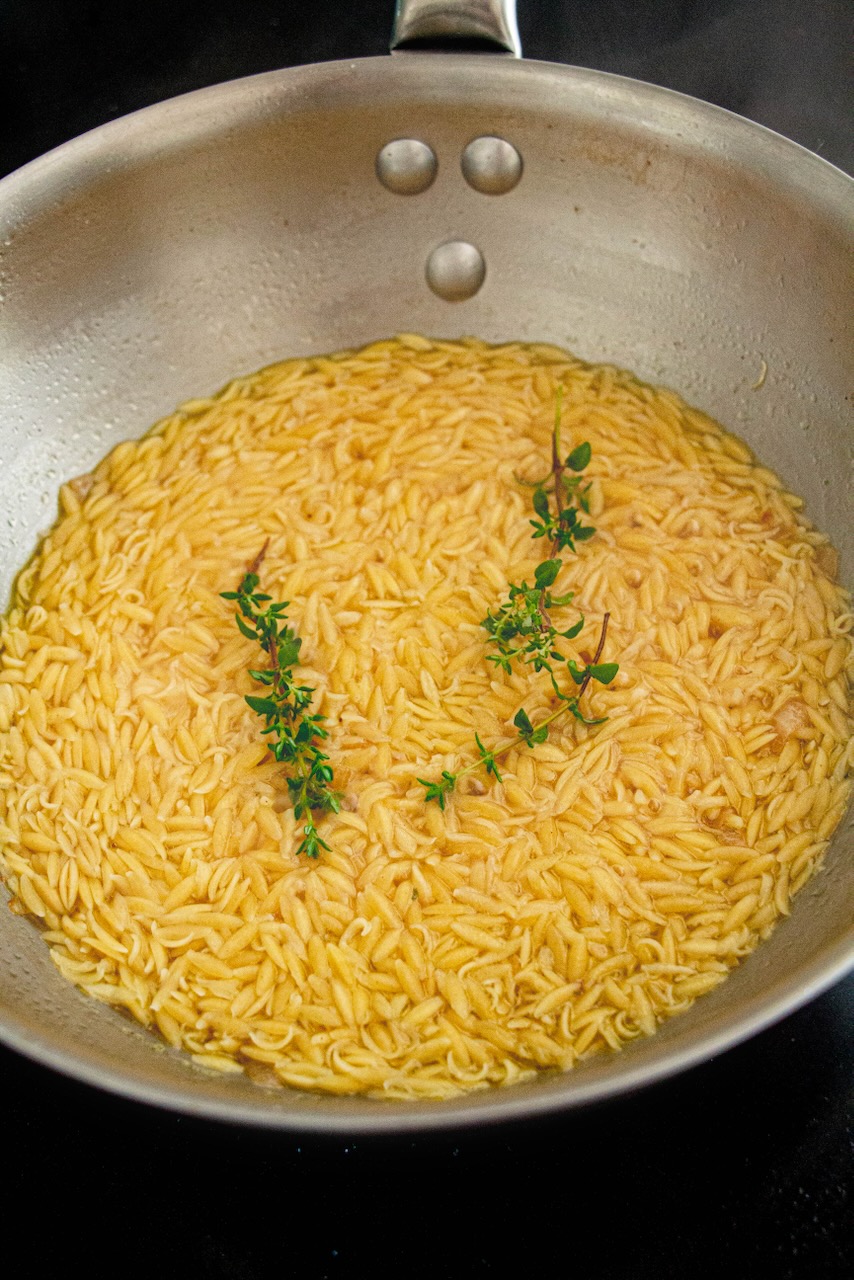 Golden orzo simmering with fresh thyme sprigs, close-up view