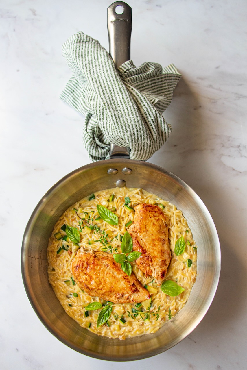 Skillet with creamy orzo, golden chicken, and basil leaves, orzo recipe