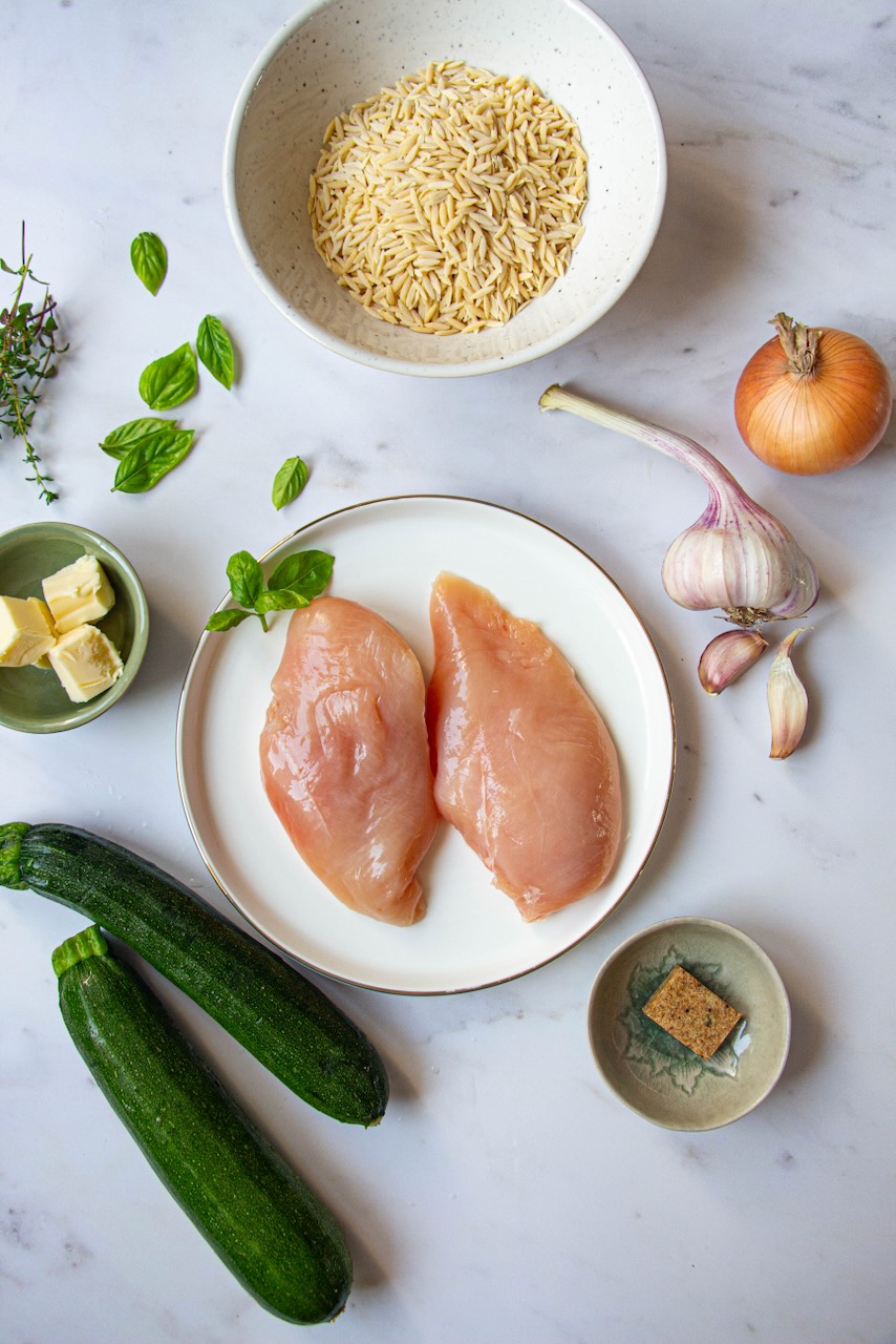 Fresh ingredients for the creamy orzo with chicken and zucchini recipe on a marbled background