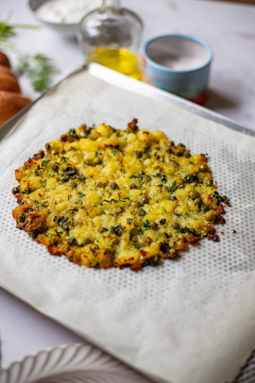 Golden potato tart base topped with herbs on parchment paper