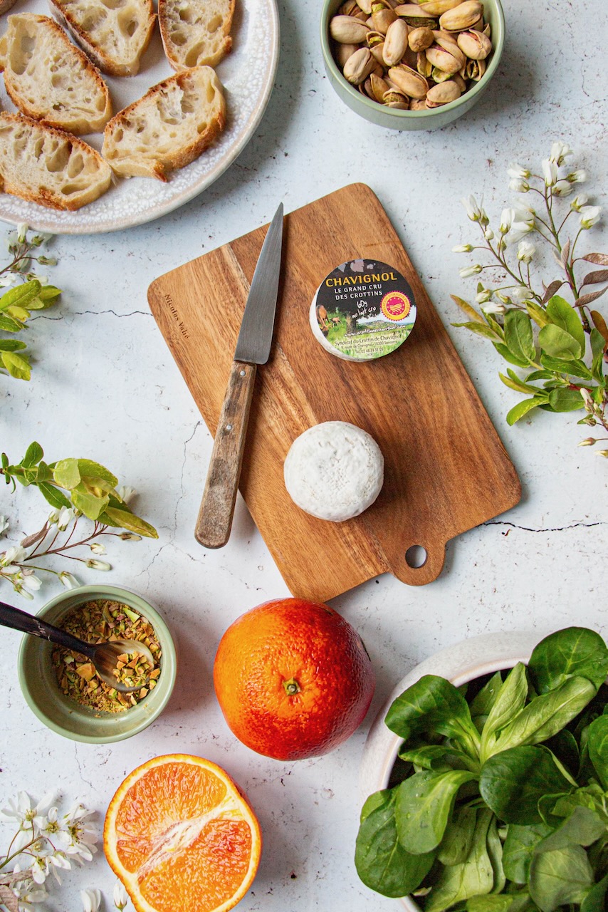 Slices of bread, Crottin de Chavignol, orange, and pistachios on a wooden board