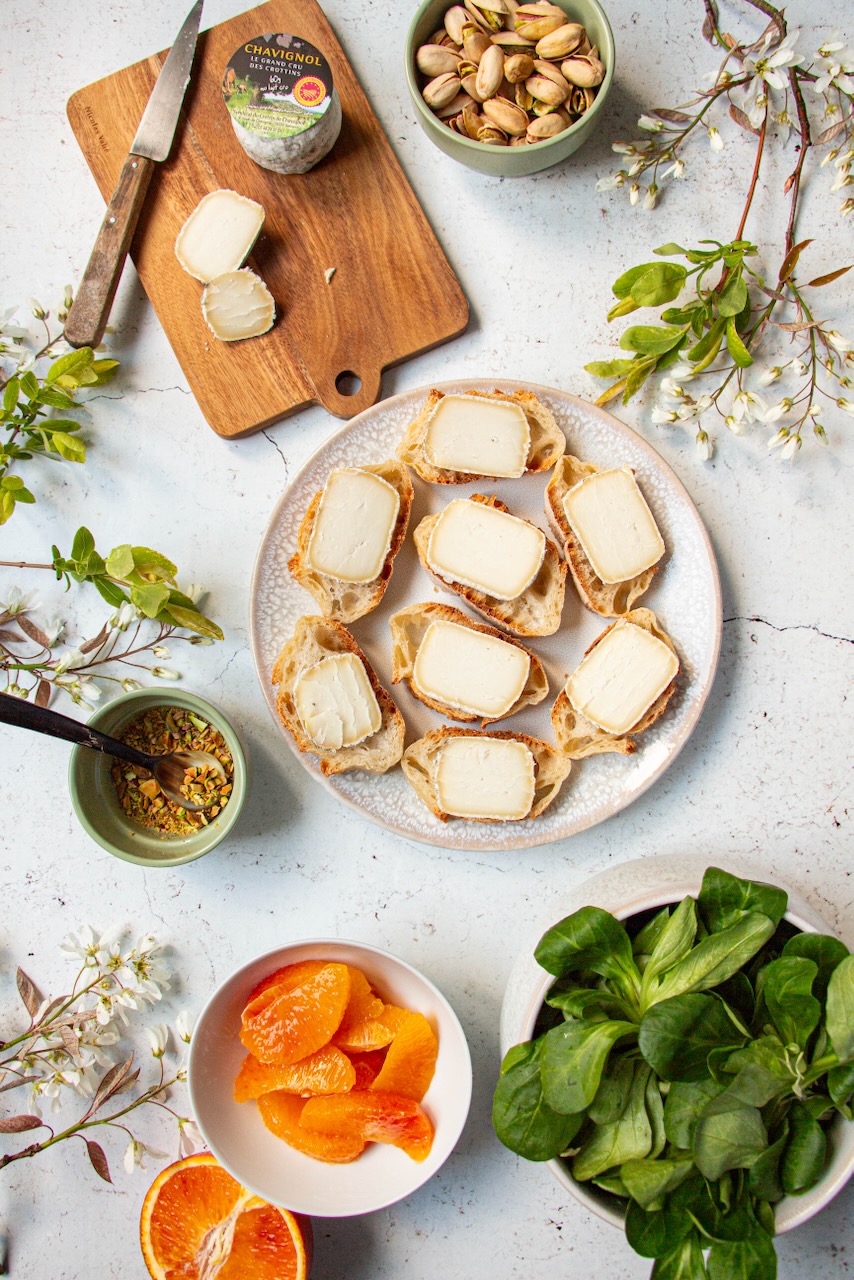 Sliced bread with Crottin de Chavignol on a plate, surrounded by colorful ingredients
