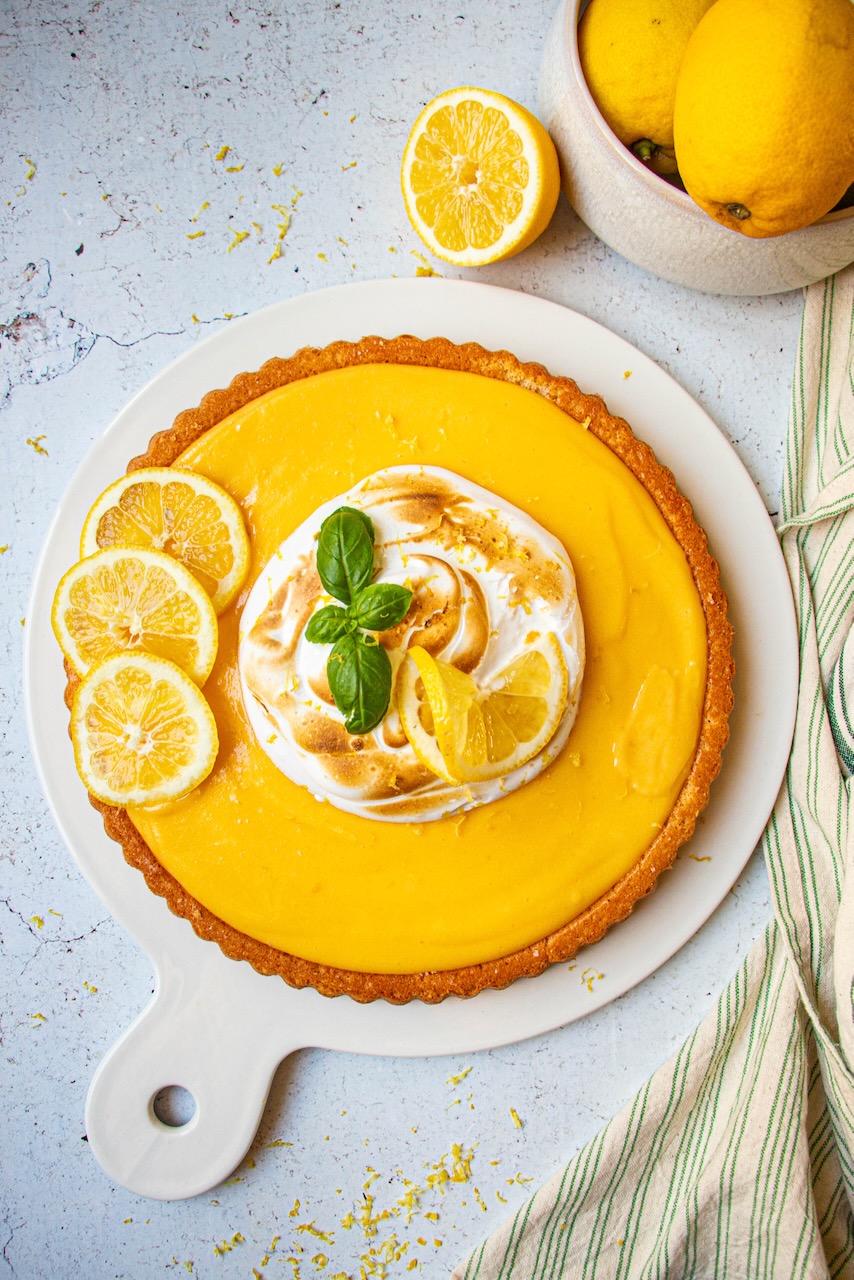 Lemon meringue cake on a white plate, decorated with lemon slices and basil