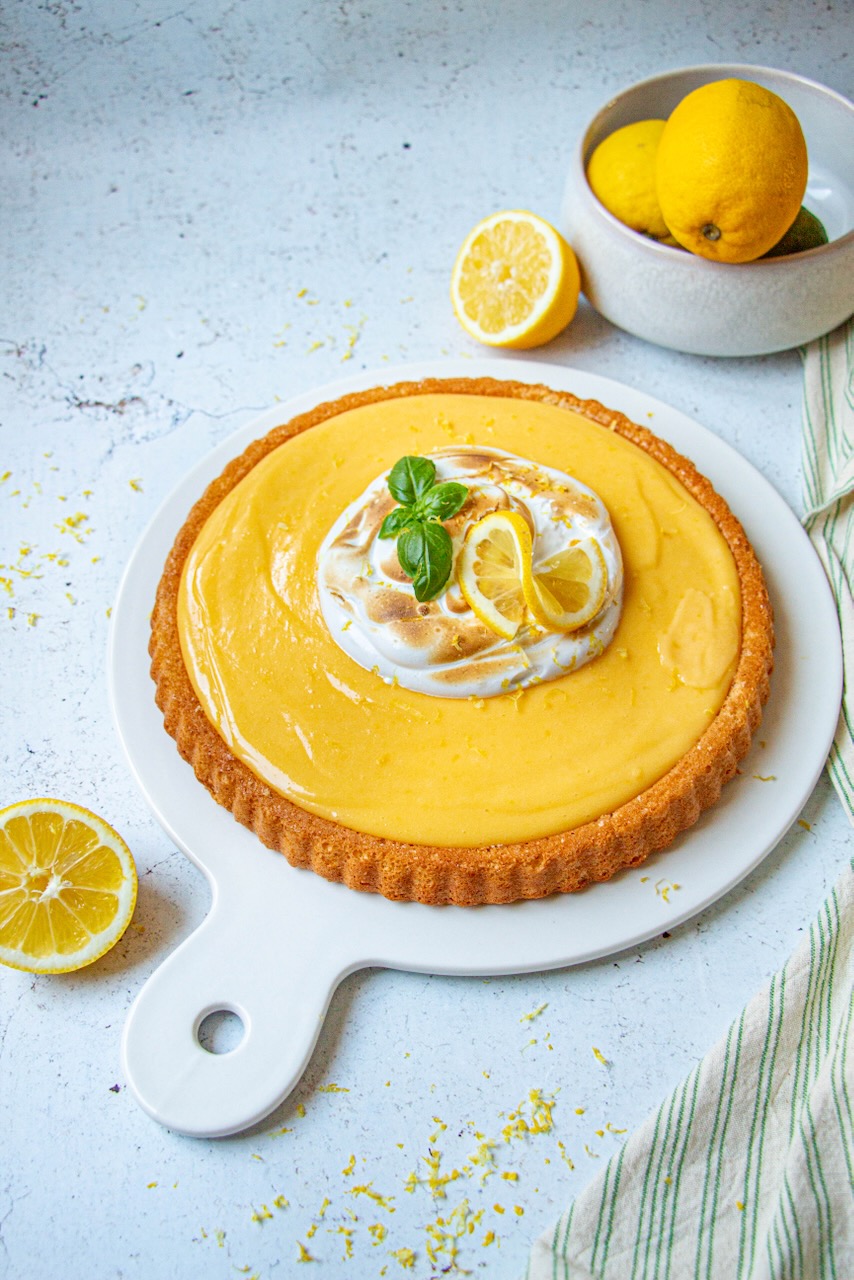 Lemon meringue cake topped with zest and mint leaves on a white plate