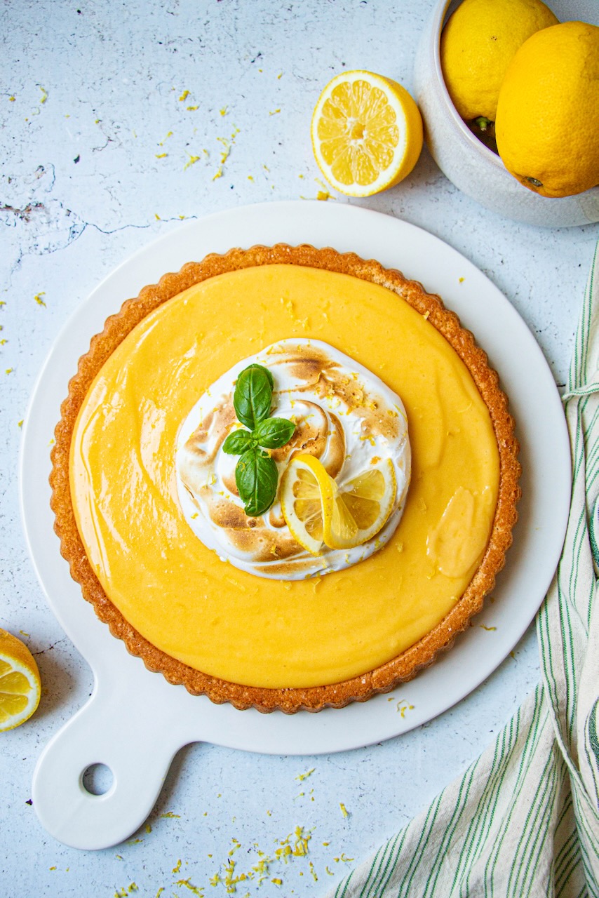 Lemon meringue cake on a white plate, garnished with lemon slices and mint leaves
