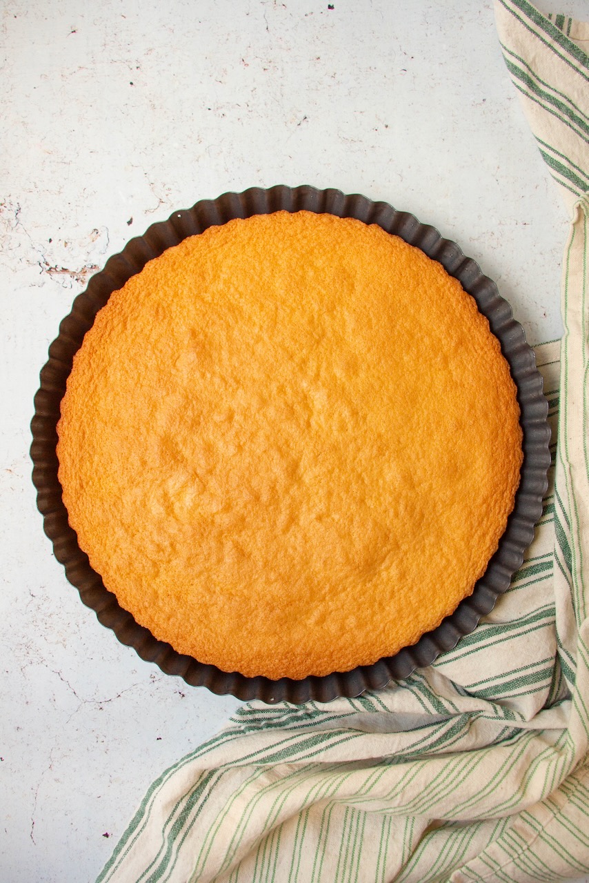 Close-up of a golden cake base in a black tart pan on a striped cloth