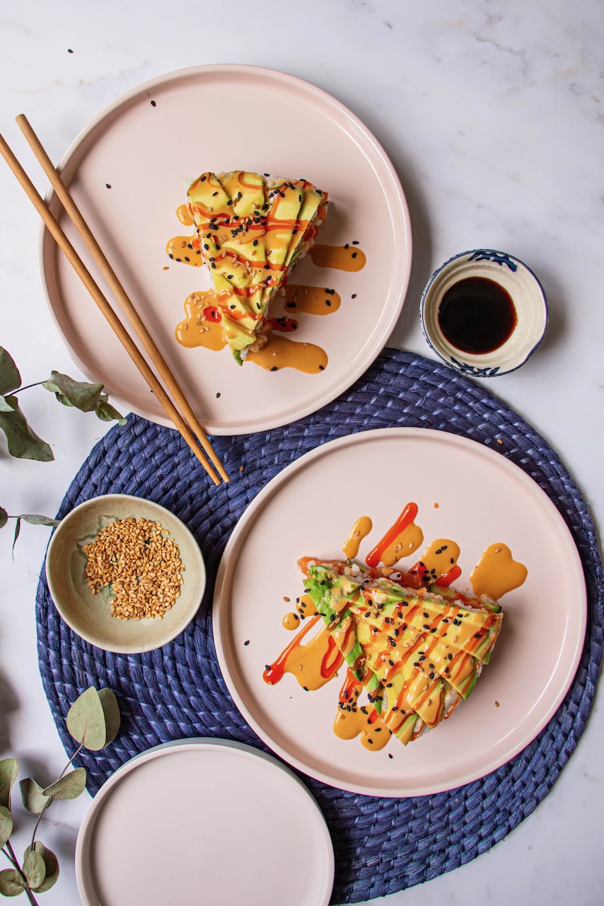 Two slices of Avocado Salmon Sushi Cake on pink plates, adorned with colorful sauces