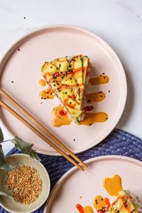 Slice of Avocado Salmon Sushi Cake topped with avocado and orange sauce, viewed from above