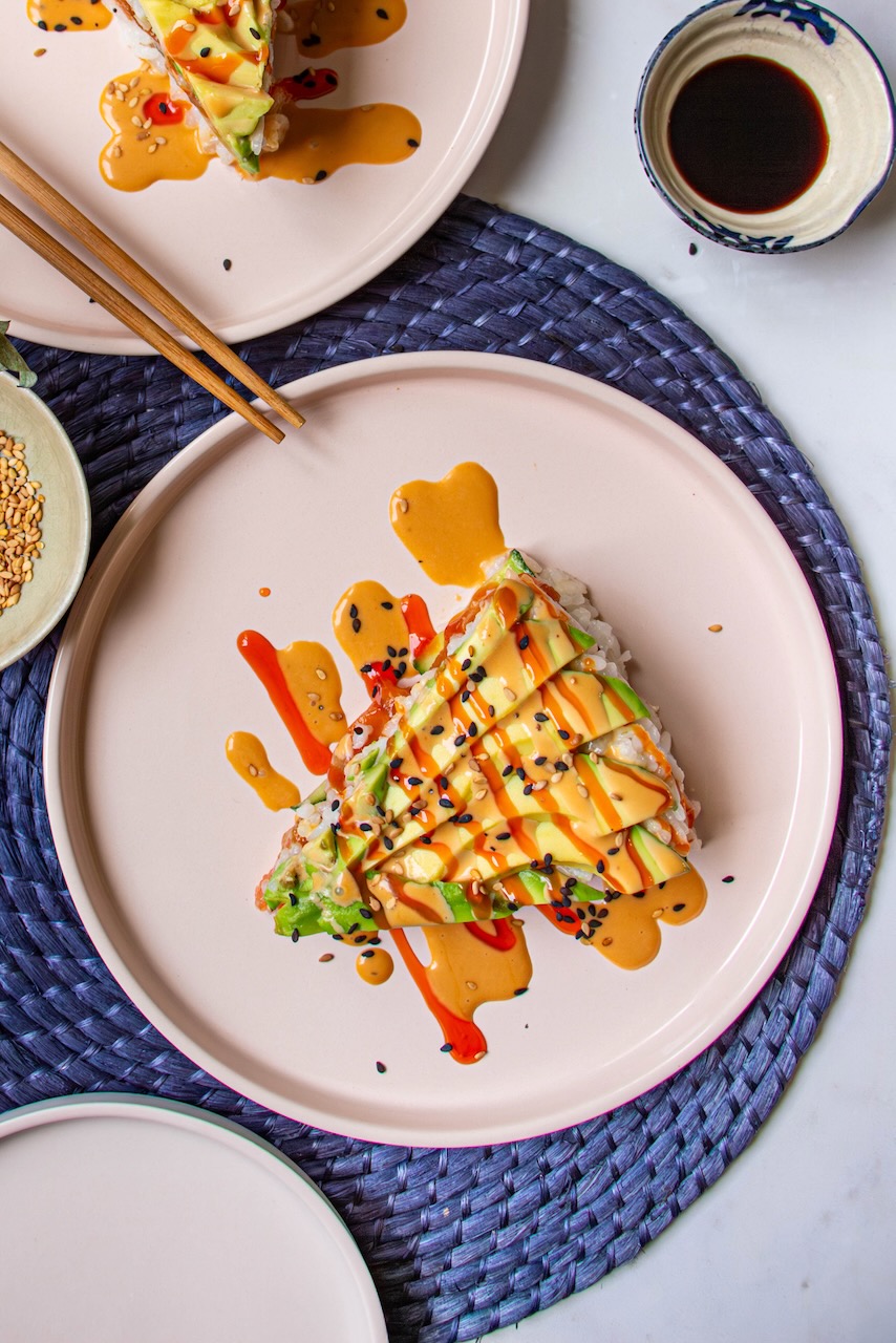 Slice of Avocado Salmon Sushi Cake drizzled with colorful sauces, on a pink plate