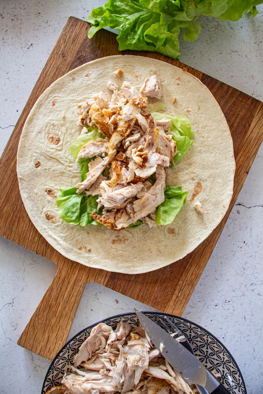 Tortilla filled with lettuce and pieces of roasted chicken on a wooden board