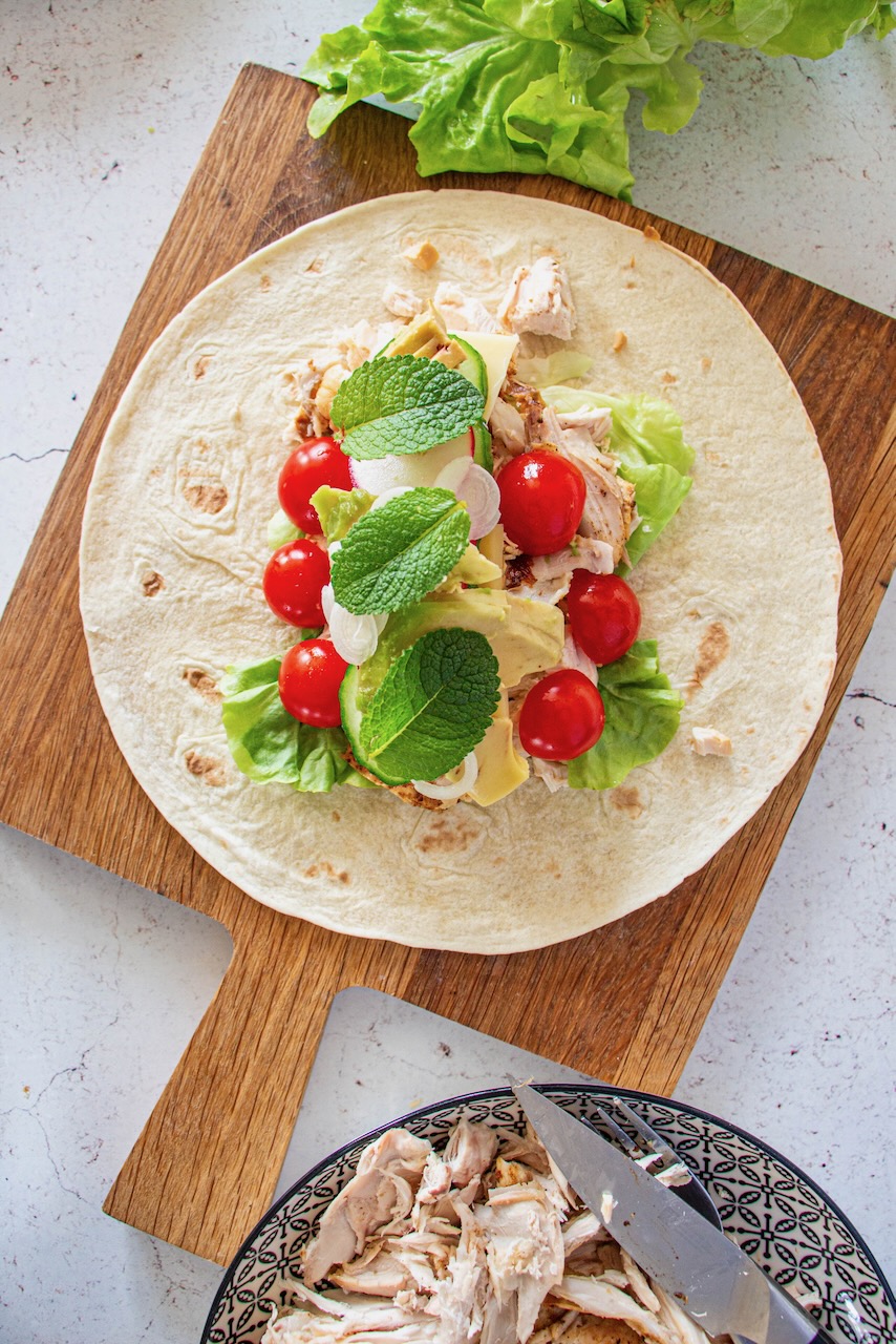 Tortilla filled with roasted chicken, lettuce, cherry tomatoes, and mint on a board
