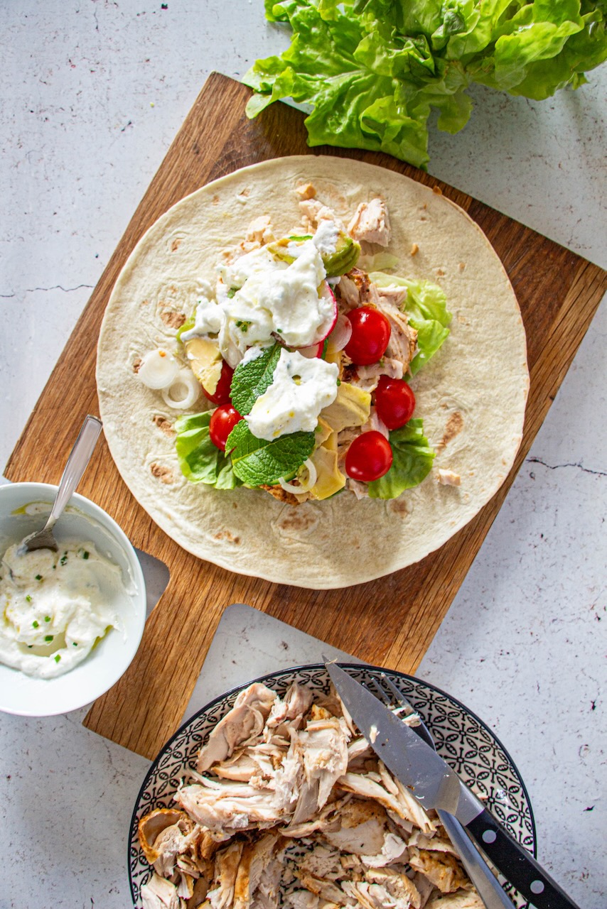 Open wrap with roasted chicken, cherry tomatoes, lettuce, and white sauce on a wooden board