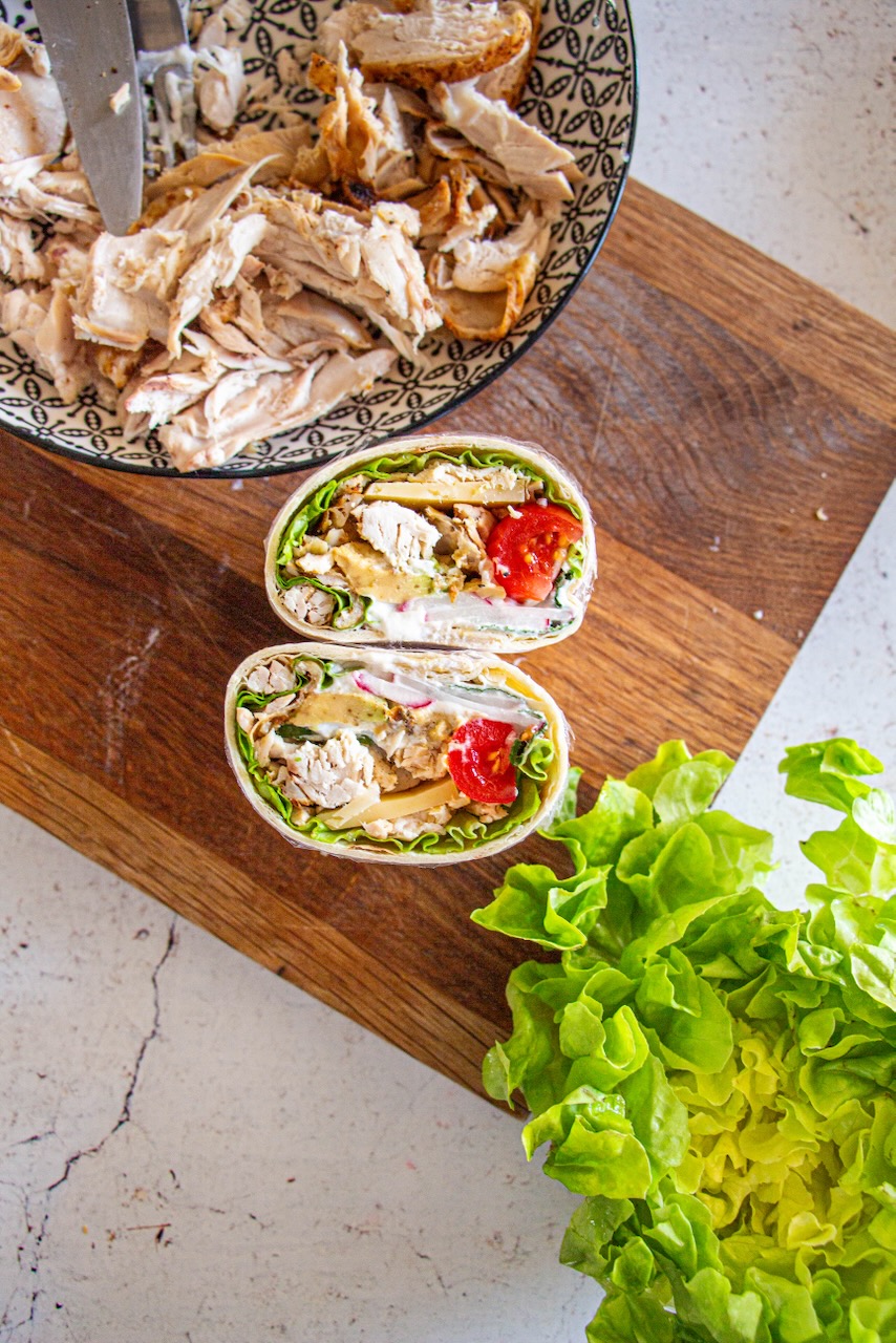 Roasted chicken protein wrap cut in half, presented on a wooden board with lettuce and shredded chicken