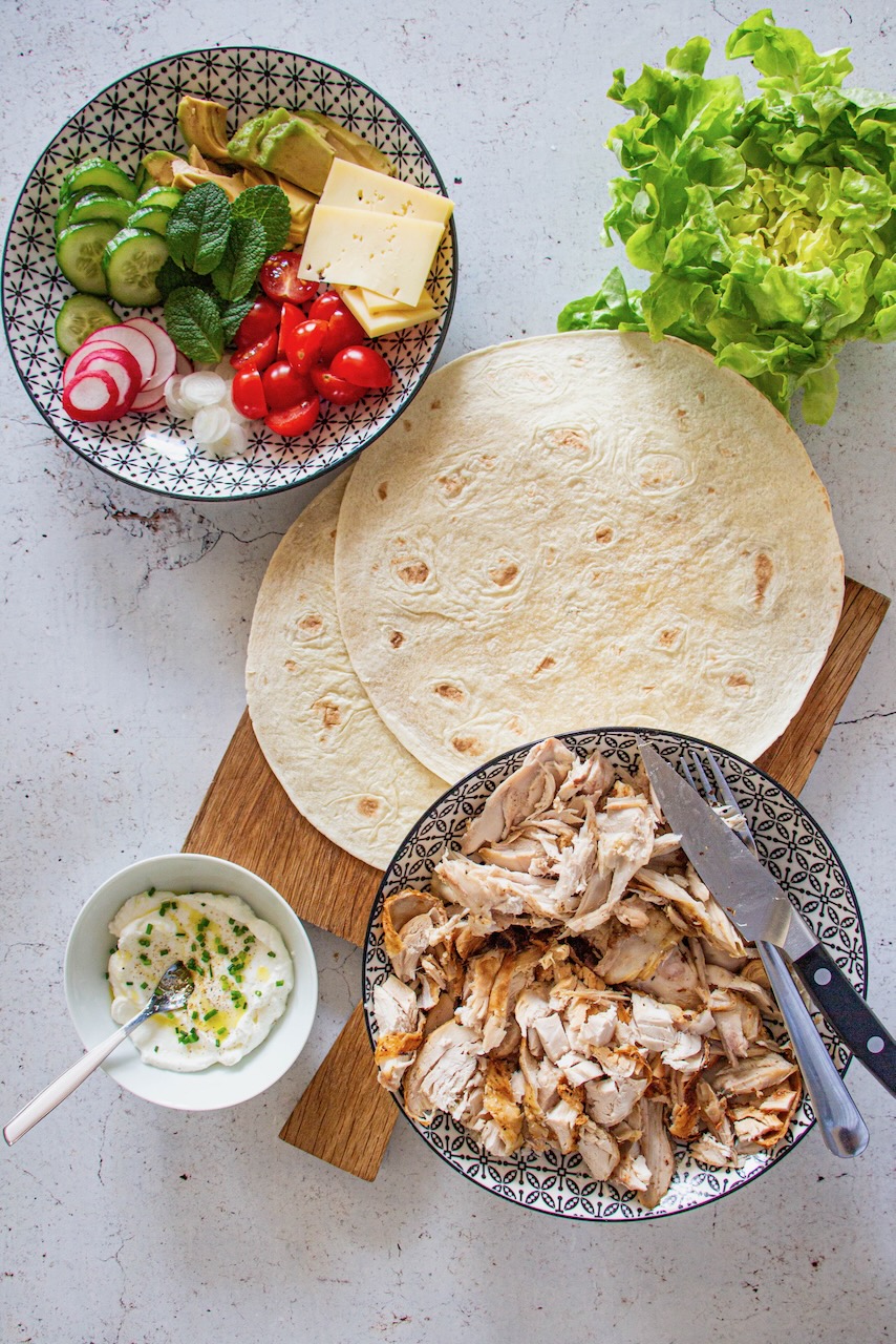 Ingredients for roasted chicken protein wrap on a wooden board, overhead view